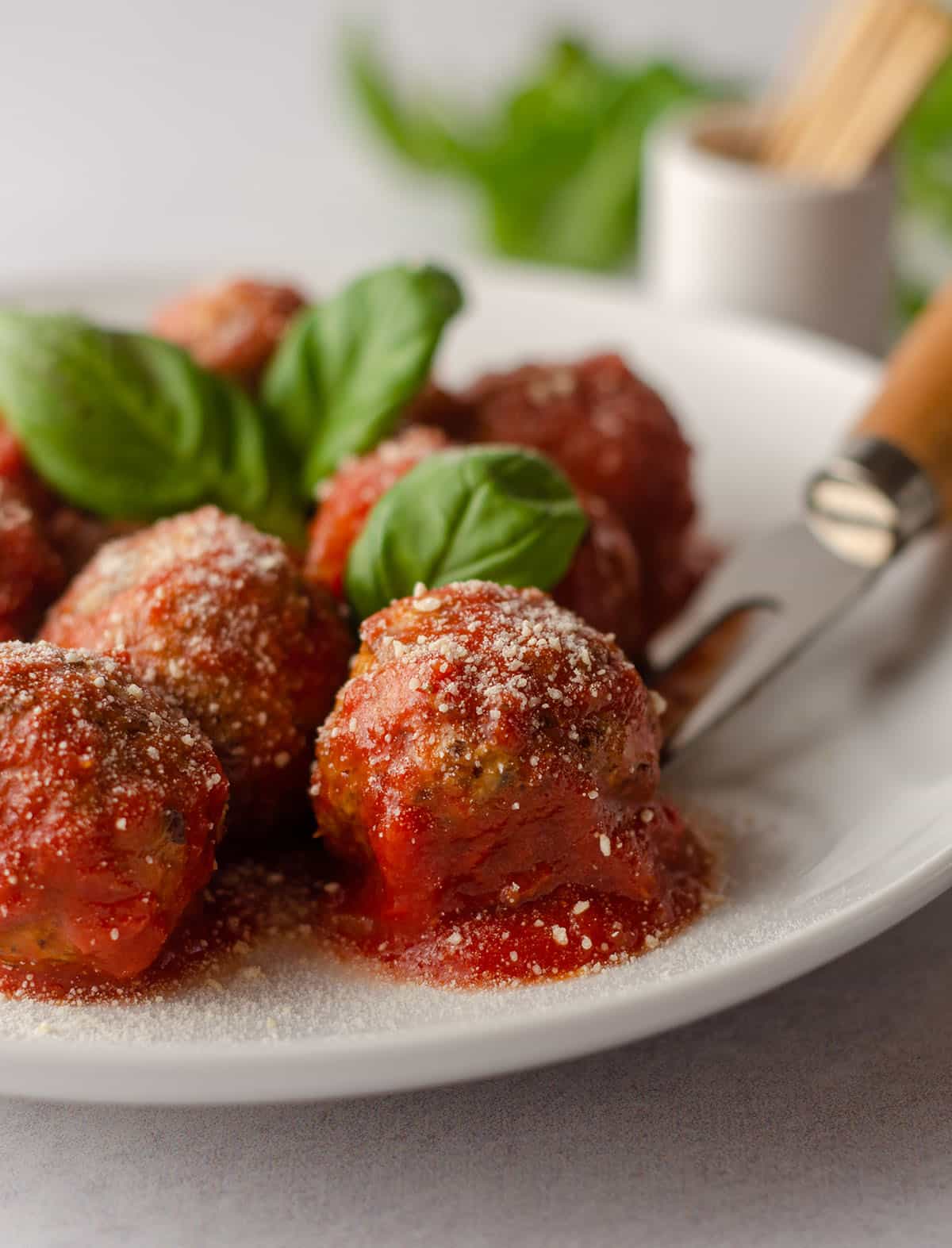 gluten free meatballs on a plate with basil leaves and a serving fork