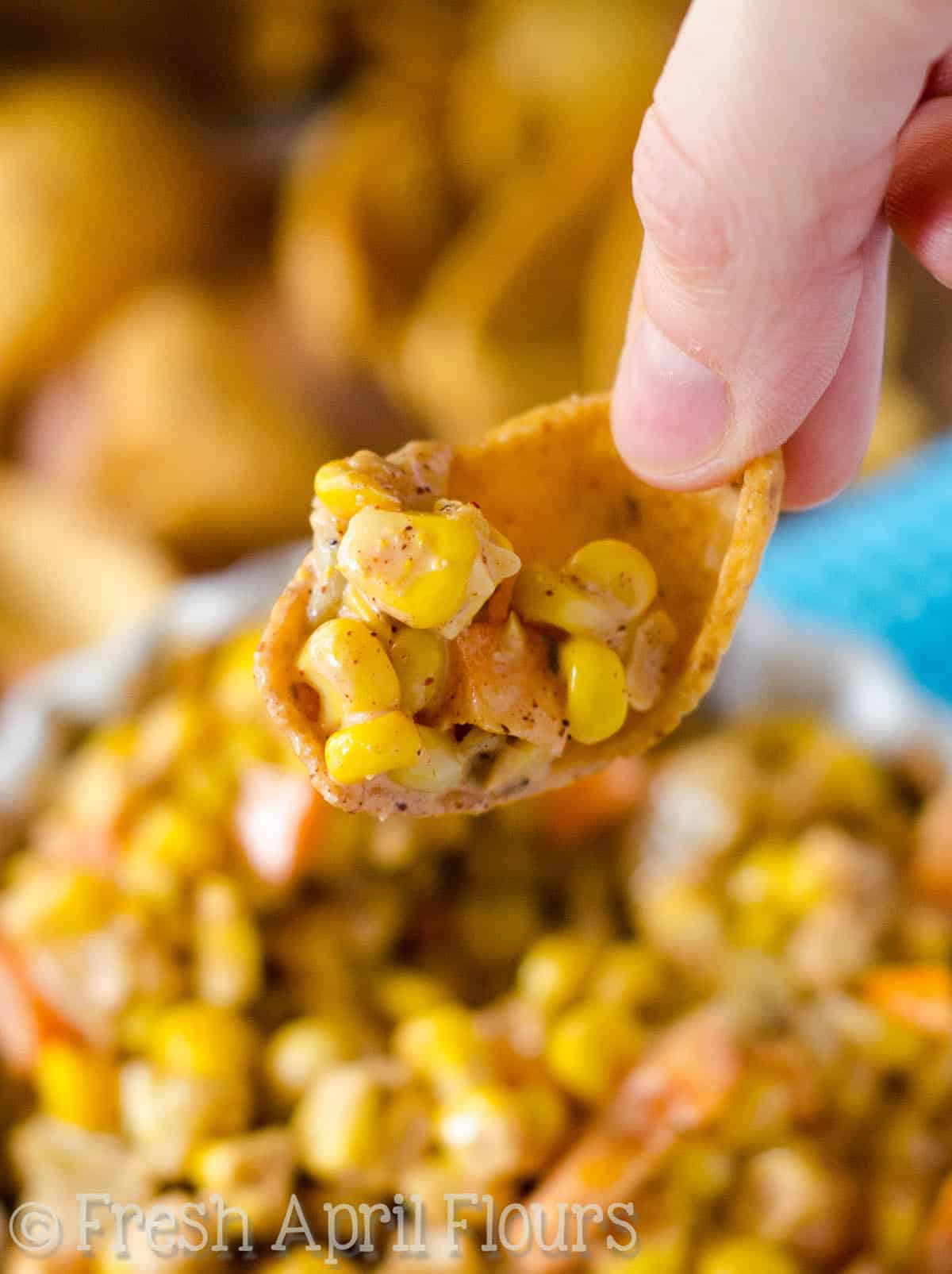 Fingers holding a corn chip with southwest corn dip on it.
