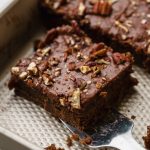 Someone is lifting a slice of chocolate Texas sheet cake out of a pan with a spatula.