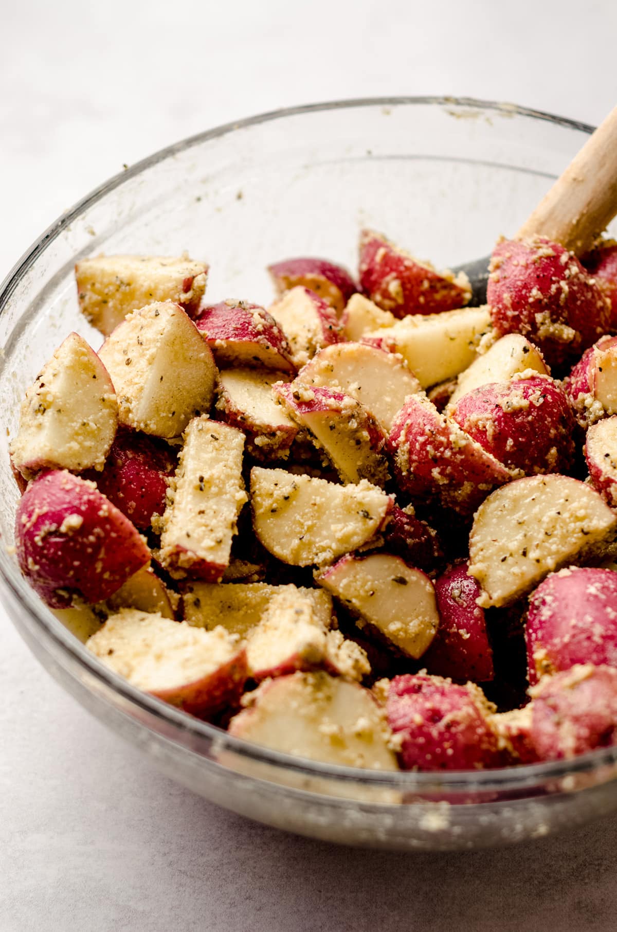 sliced red potatoes in a bowl with cheese and spices ready to be oven roasted