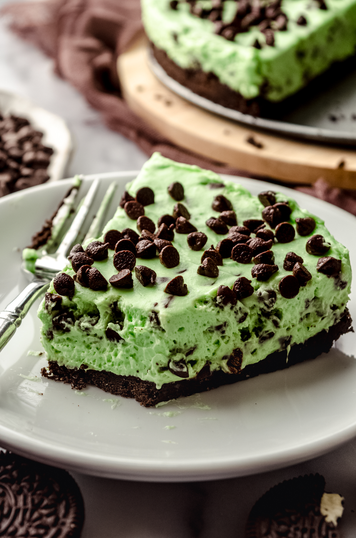 A slice of no bake mint chocolate chip pie on a plate with a fork. A bite has been taken out of it.