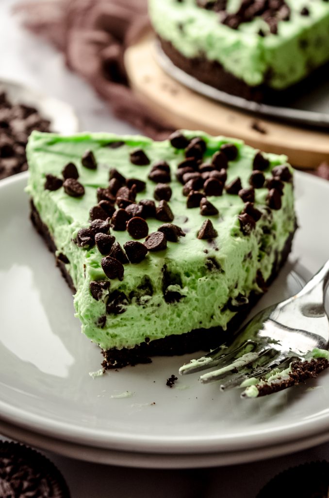 A slice of no bake mint chocolate chip pie on a plate with a fork. A bite has been taken out of it.