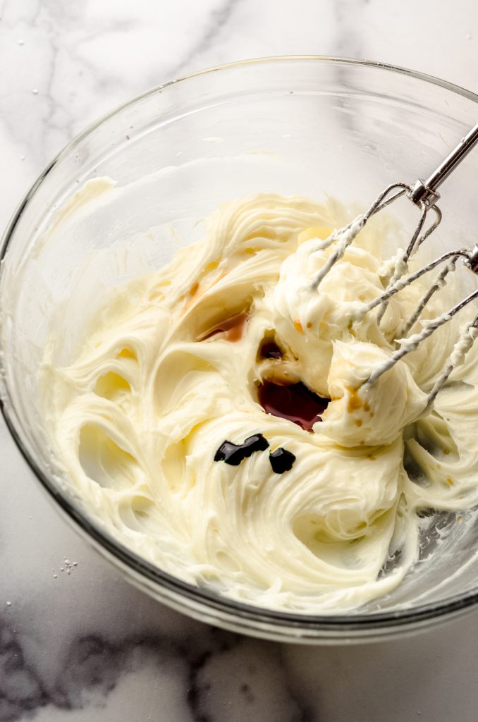 A bowl of beaten cream cheese for no bake mint chocolate chip pie with beaters in it.