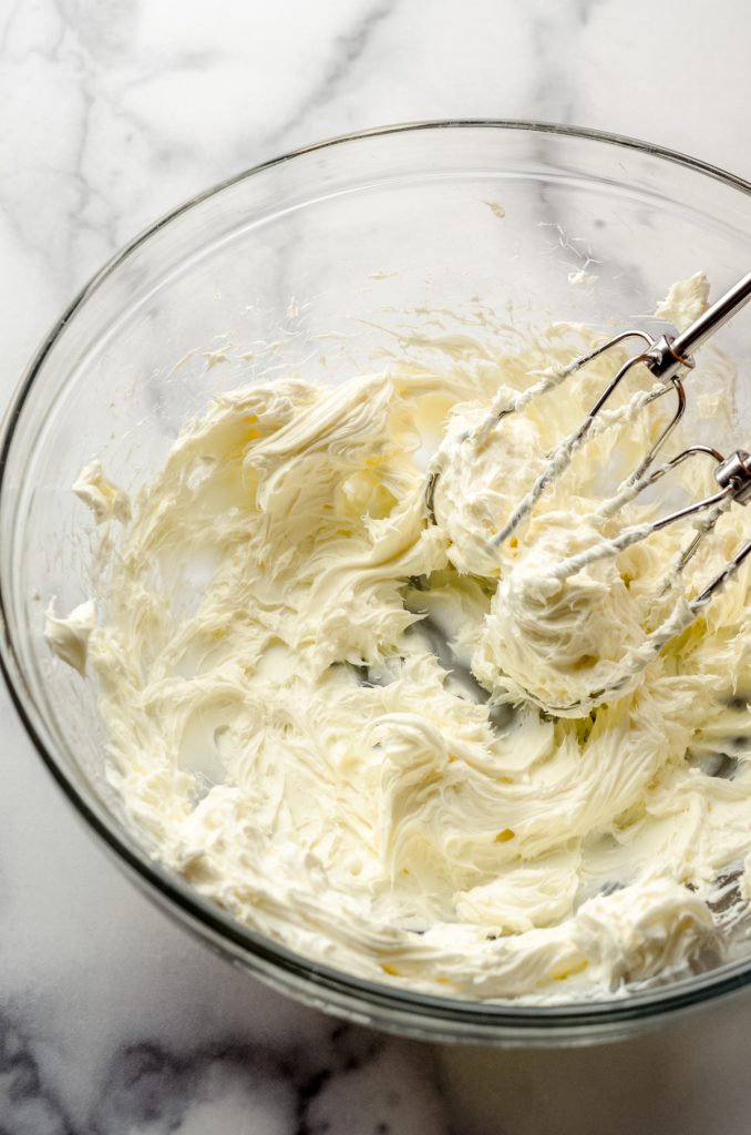 A bowl of beaten cream cheese for no bake mint chocolate chip pie with beaters in it.