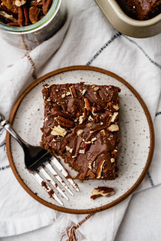 Aerial photo of a slice of chocolate Texas sheet cake on a plate with a fork and a bite taken out of the slice.