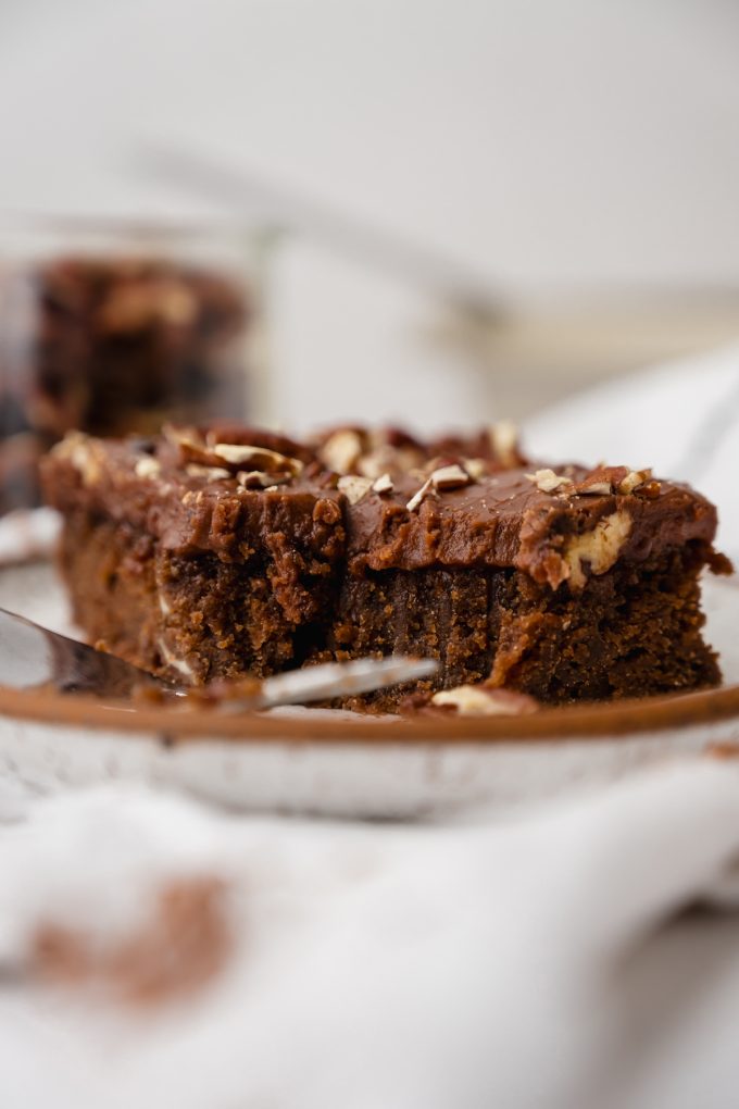 A slice of chocolate Texas sheet cake on a plate with a fork and a bite has been taken out of the cake.