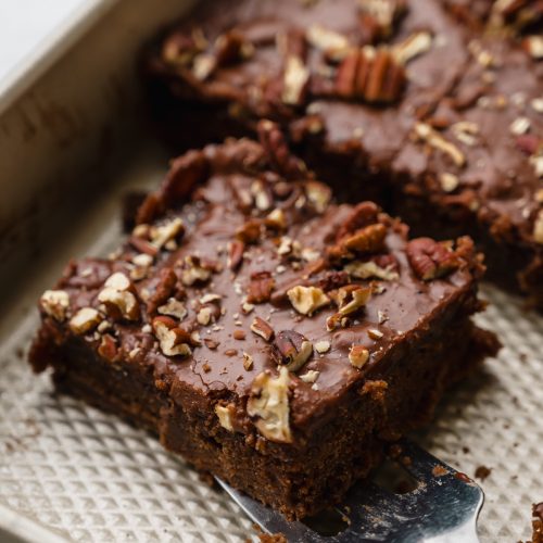 Someone is lifting a slice of chocolate Texas sheet cake out of a pan with a spatula.