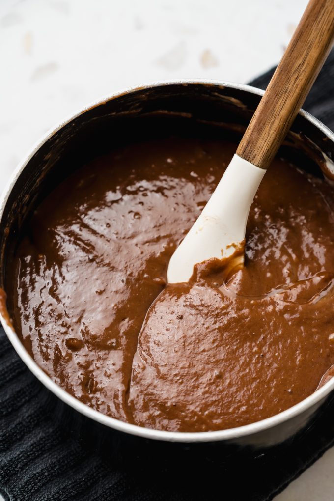 A saucepan of a mixture for the batter of a Texas sheet cake being stirred together with a spatula.