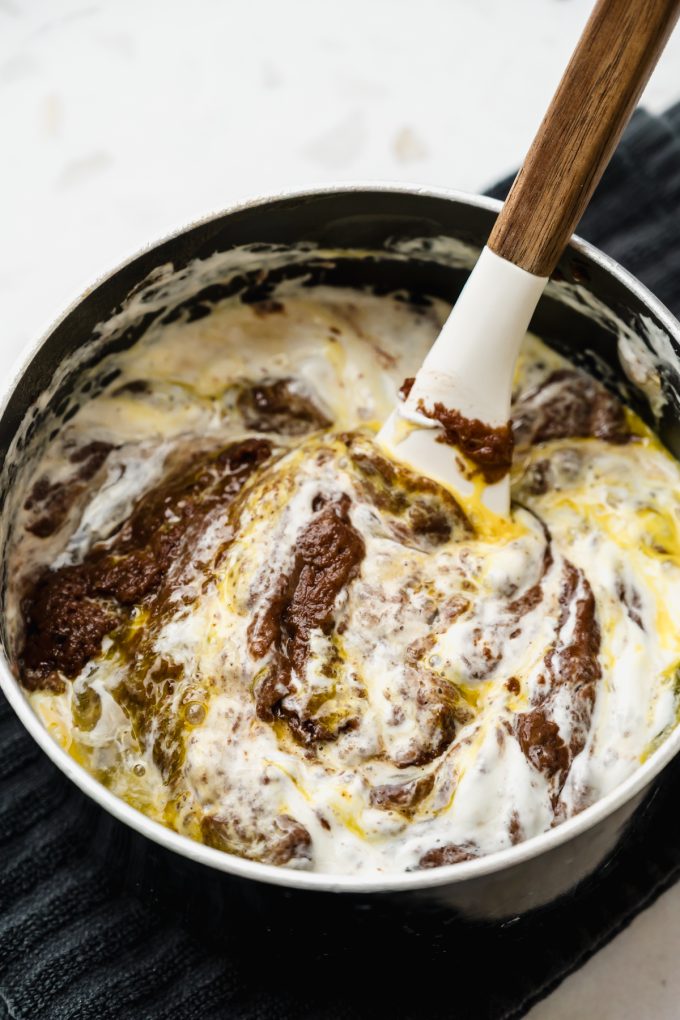 A saucepan of a mixture for the batter of a Texas sheet cake being stirred together with a spatula.