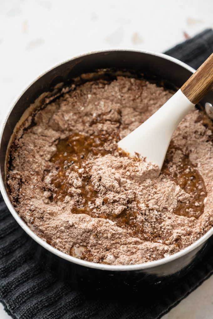 A saucepan of a mixture for the batter of a Texas sheet cake being stirred together with a spatula.