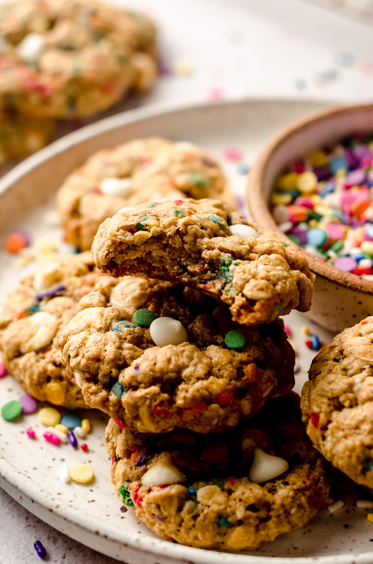 funfetti oatmeal cookies on a plate with a bowl of sprinkles and one cookie has a bite taken out of it