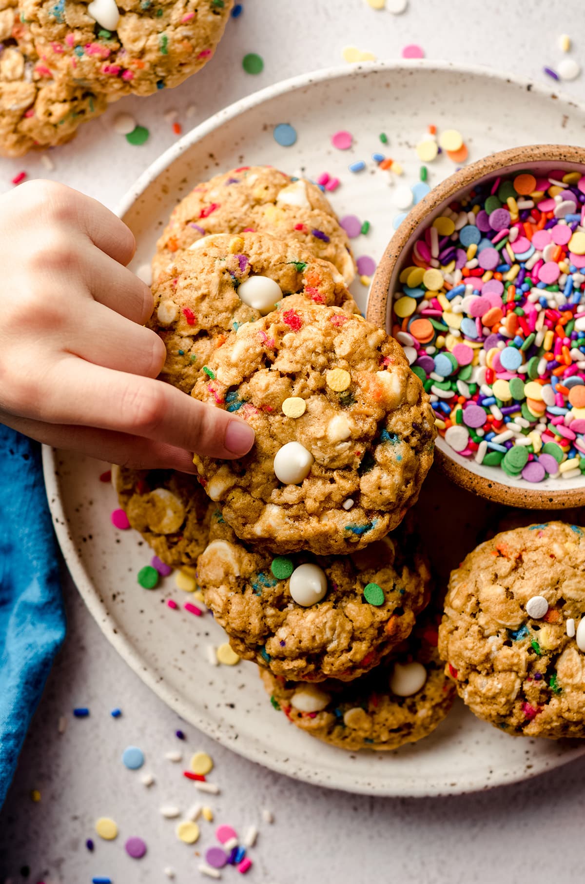 aerial photo of a child's fingers picking up a funfetti oatmeal cookie up from a plate of cookies