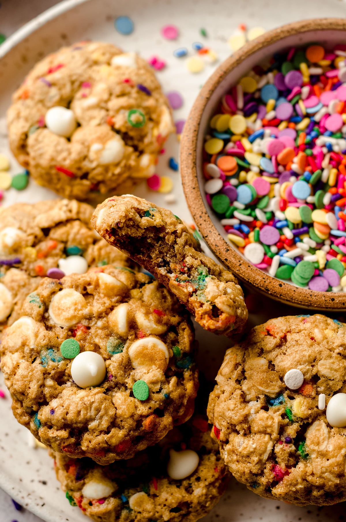 funfetti oatmeal cookies on a plate with a bowl of sprinkles and one cookie has a bite taken out of it