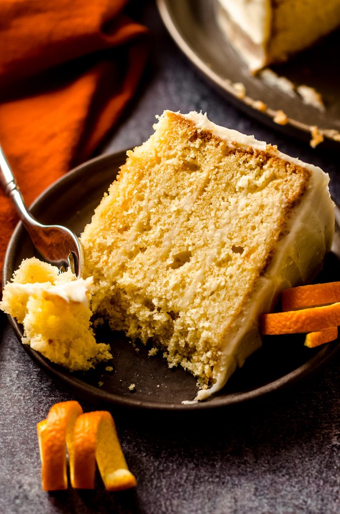 slice of orange creamsicle layer cake on a plate with a fork and a bite taken out of it