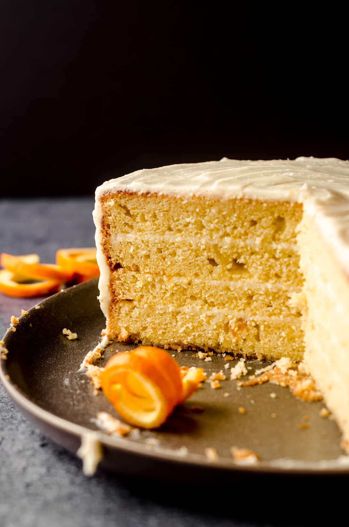 sliced orange creamsicle layer cake on a plate with exposed layers and curled orange peel