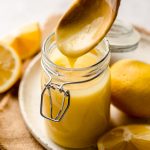 a wooden spoon dripping lemon curd back into a jar