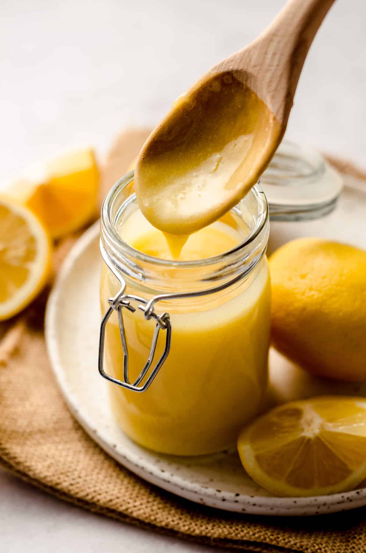 a wooden spoon dripping lemon curd back into a jar