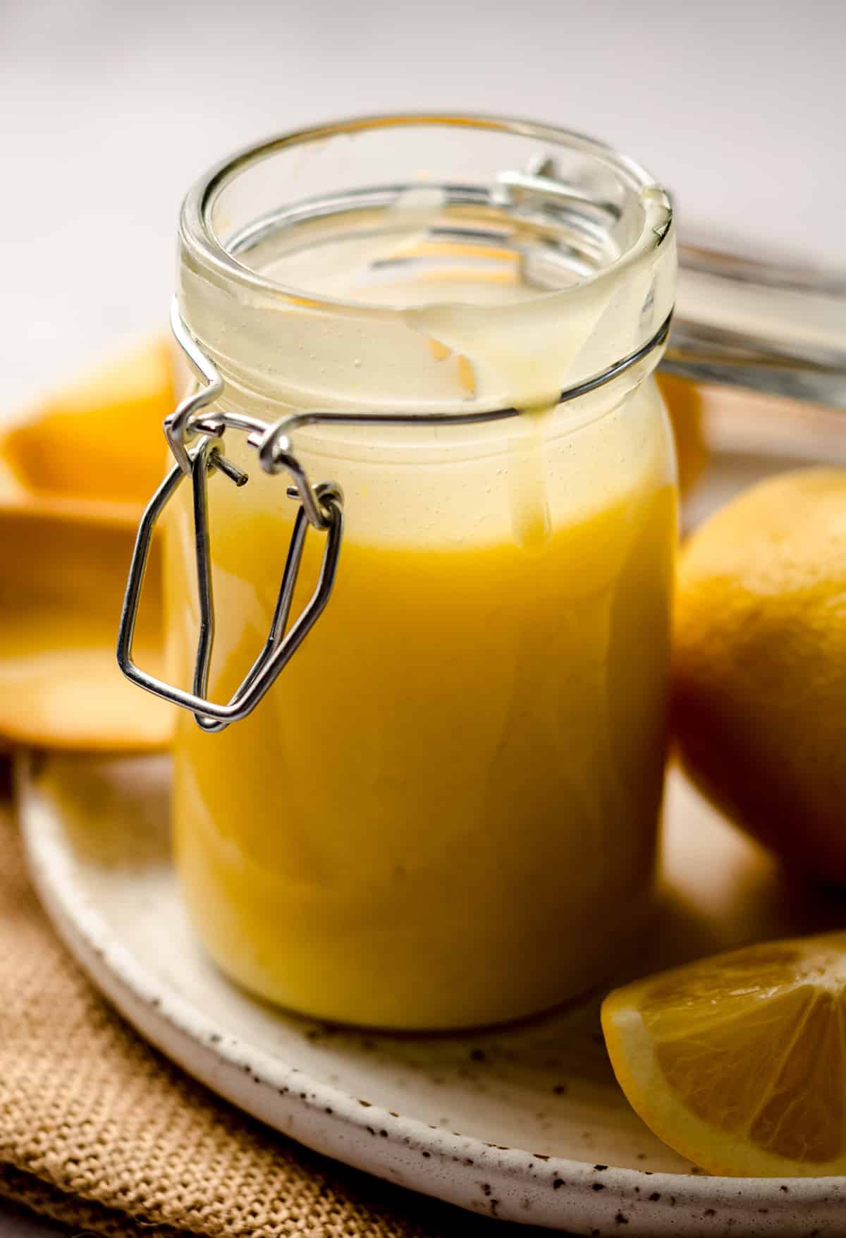a jar of lemon curd on a plate with lemons