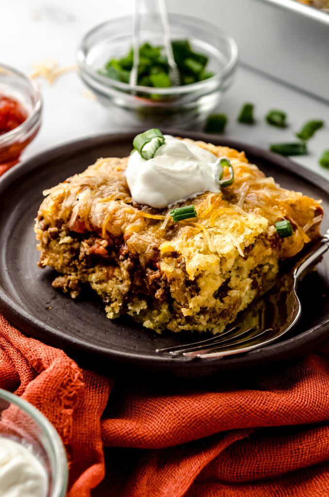 A slice of taco casserole on a plate with a fork.