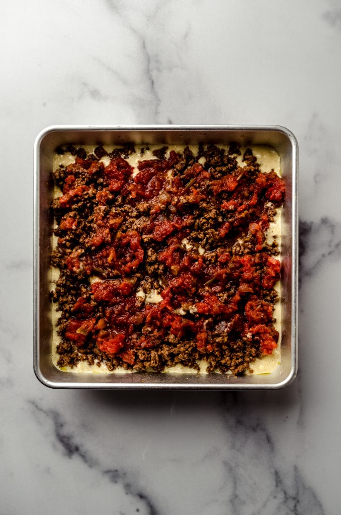 Aerial photo of the salsa layer on top of the meat and cornbread layer in a taco casserole in a baking dish.