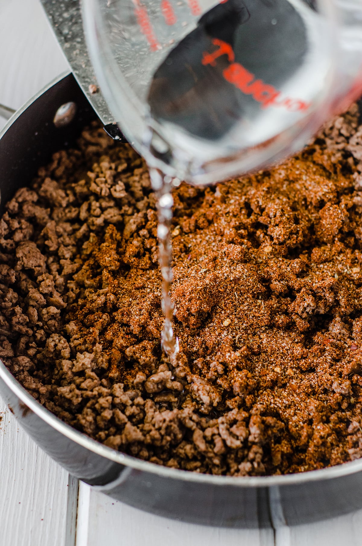 pouring water into browned meat with taco seasoning