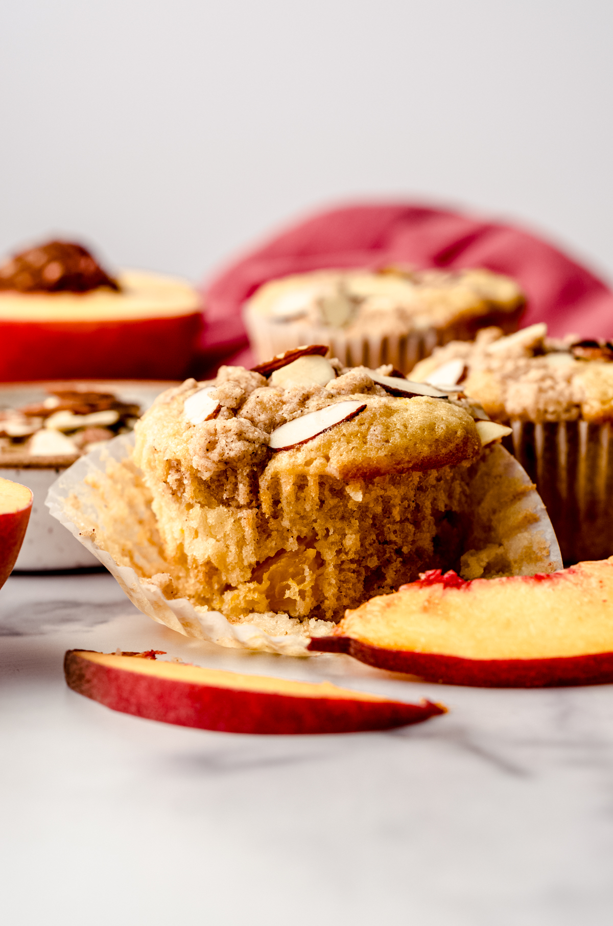 A peach almond streusel muffin sitting on a surface with peaches and almond slices around it.