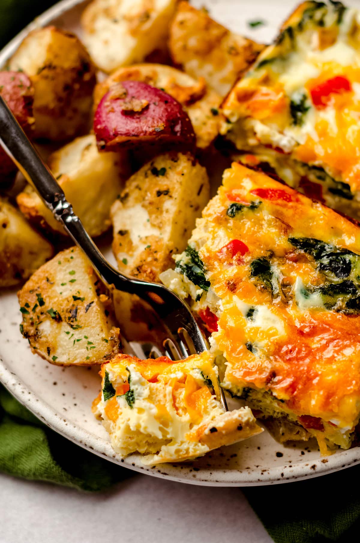 slice of breakfast casserole on a plate with a fork and breakfast potatoes