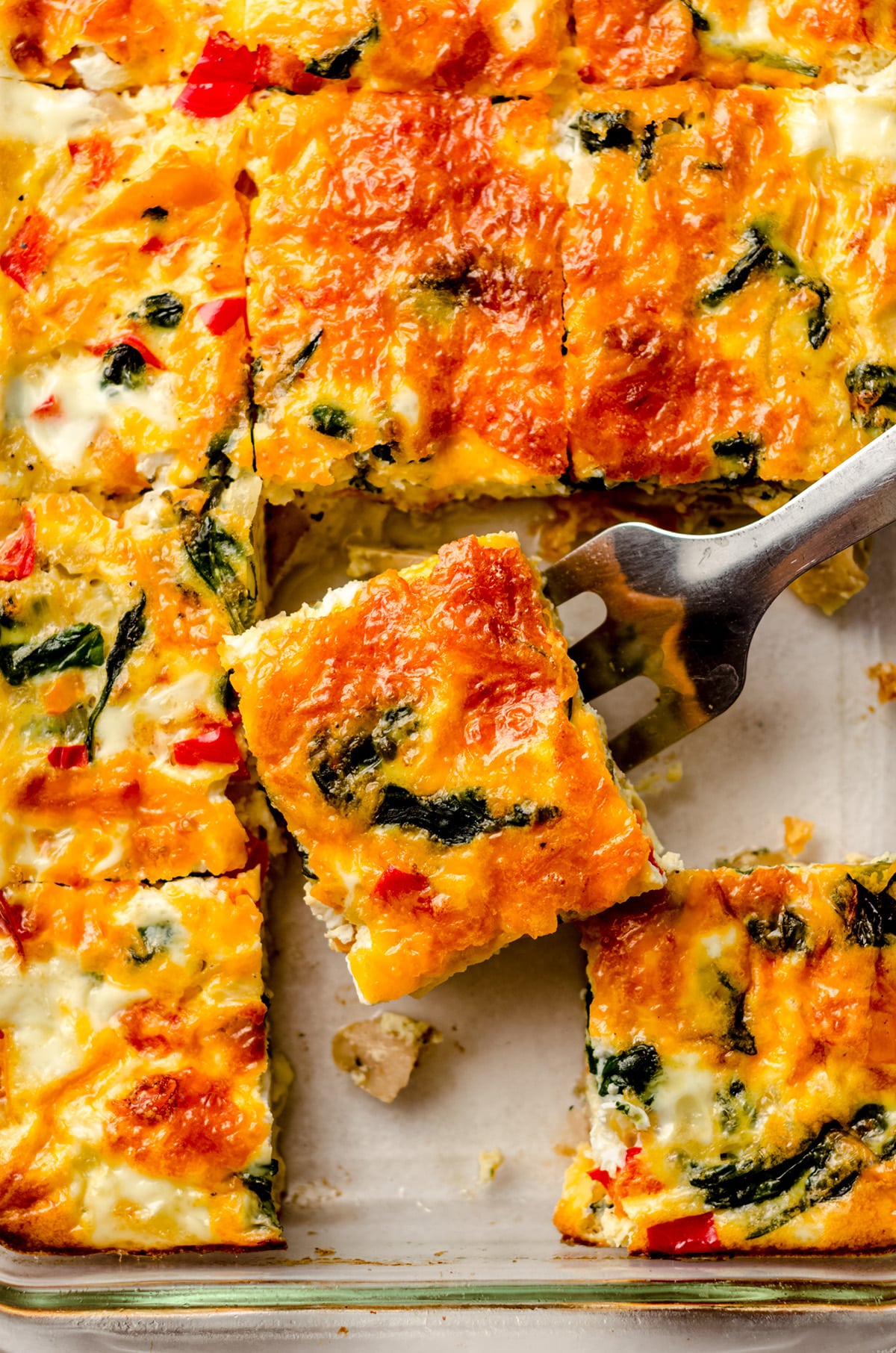 aerial photo of breakfast casserole sliced in a dish and a spatula is taking a slice out to serve it