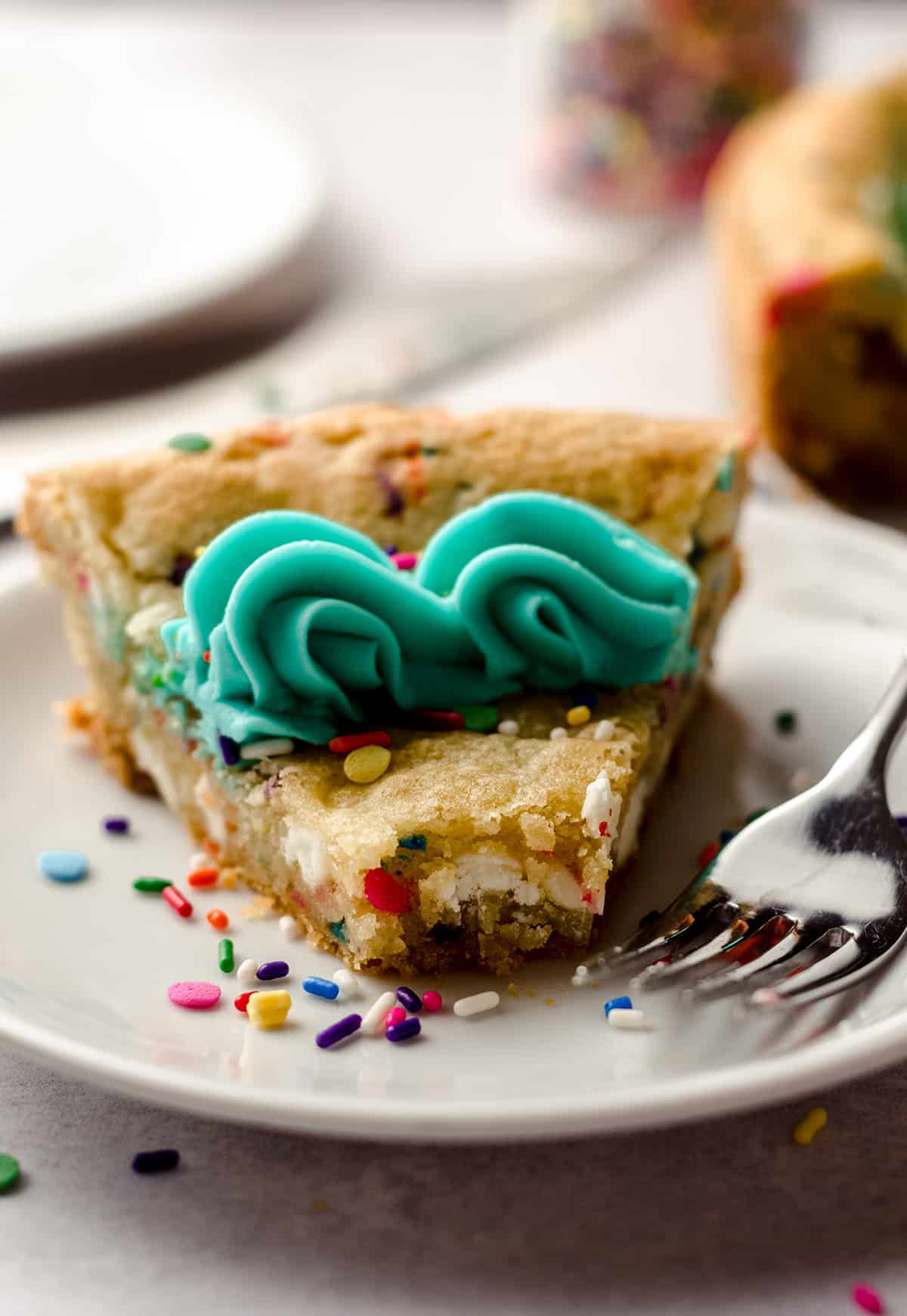 a slice of funfetti sugar cookie cake on a plate with a bite taken out of it