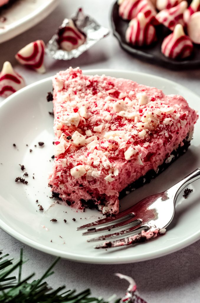 A slice of no bake peppermint pie on a plate with a fork and a bite has been taken out of the pie.