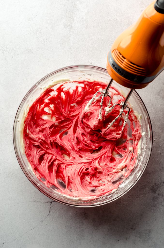 Aerial photo of cream cheese and red food coloring blended with an electric mixer.