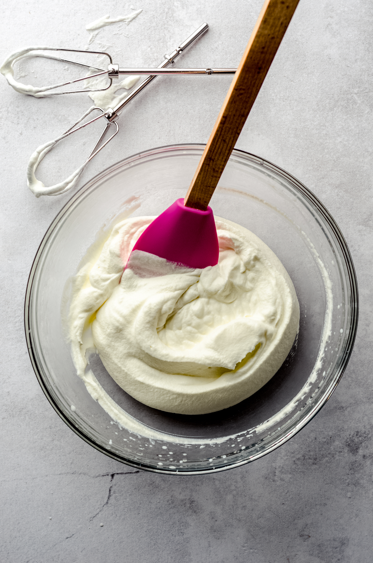 Aerial photo of a bowl of whipped cream with a pink spatula in it.
