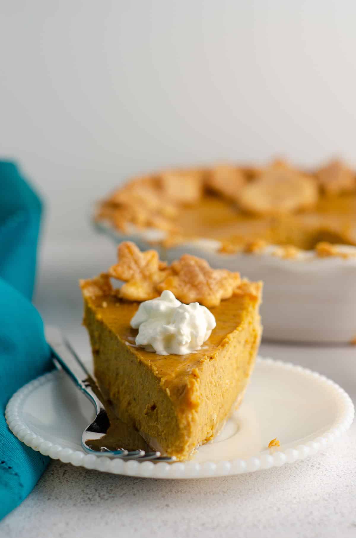 slice of pumpkin pie with a dollop of whipped cream on a plate with a fork