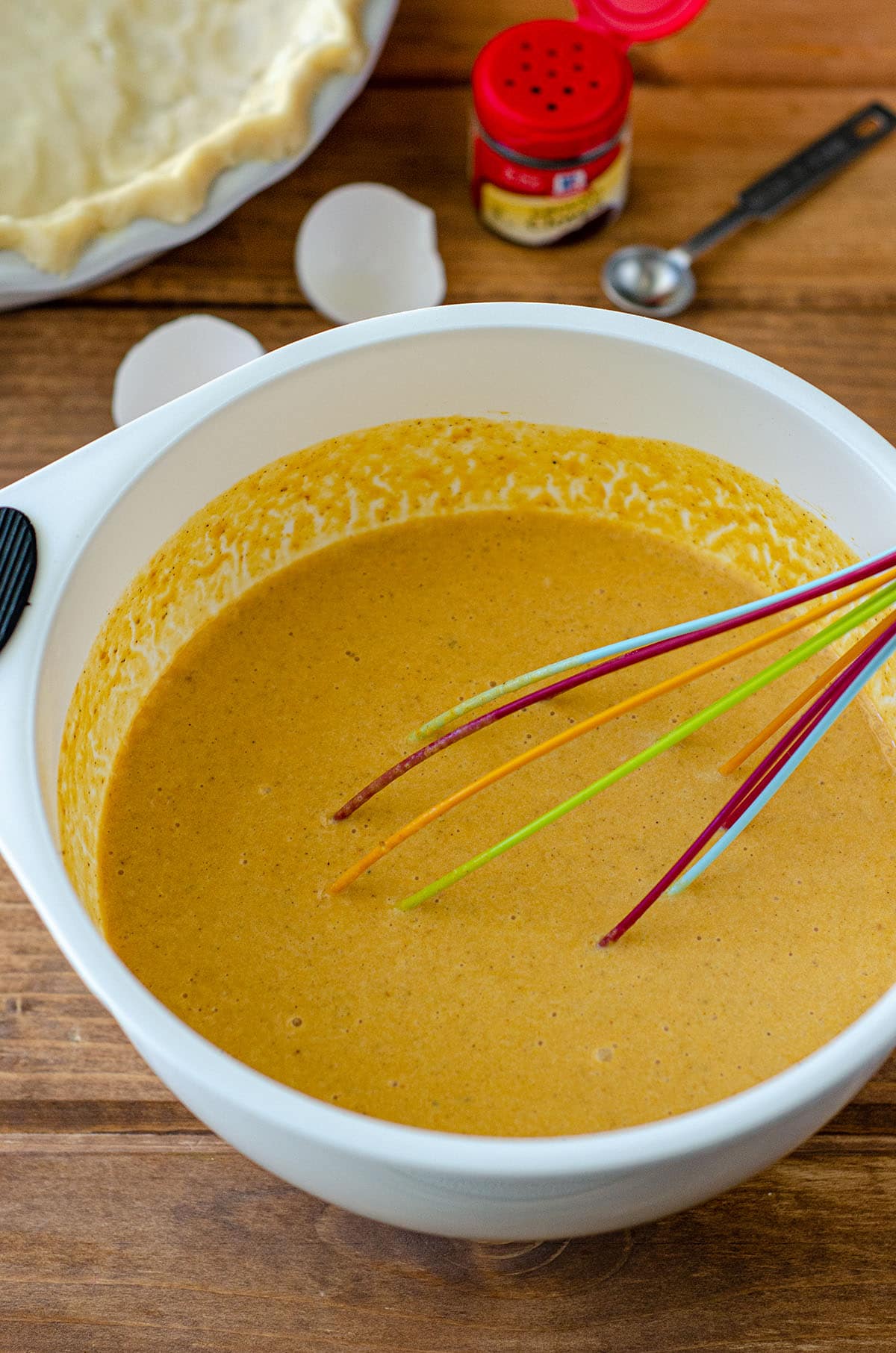 pumpkin pie filling in a bowl with a rainbow whisk ready to go into the pie crust