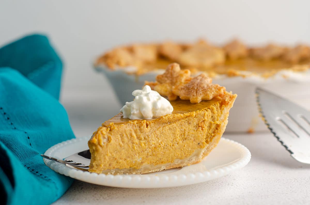 side view of slice of pumpkin pie with a dollop of whipped cream on a plate with a fork