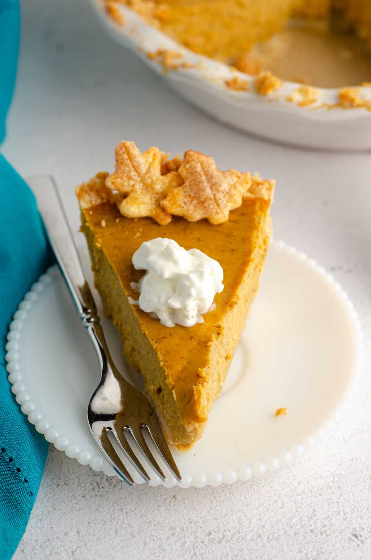 slice of pumpkin pie with a dollop of whipped cream on a plate with a fork