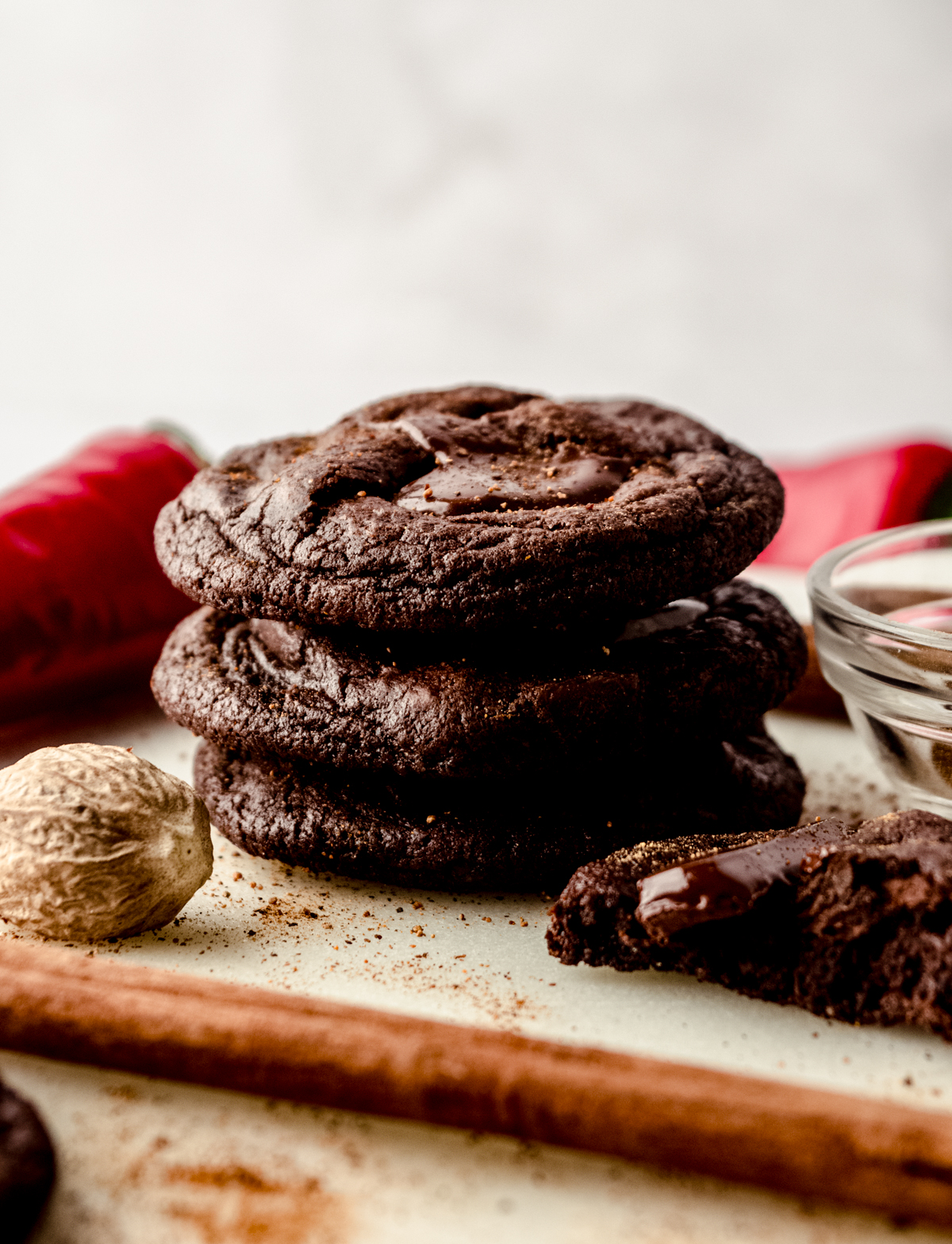 A stack of chocolate cayenne cookies with chili peppers, nutmeg, and cinnamon sticks around it.