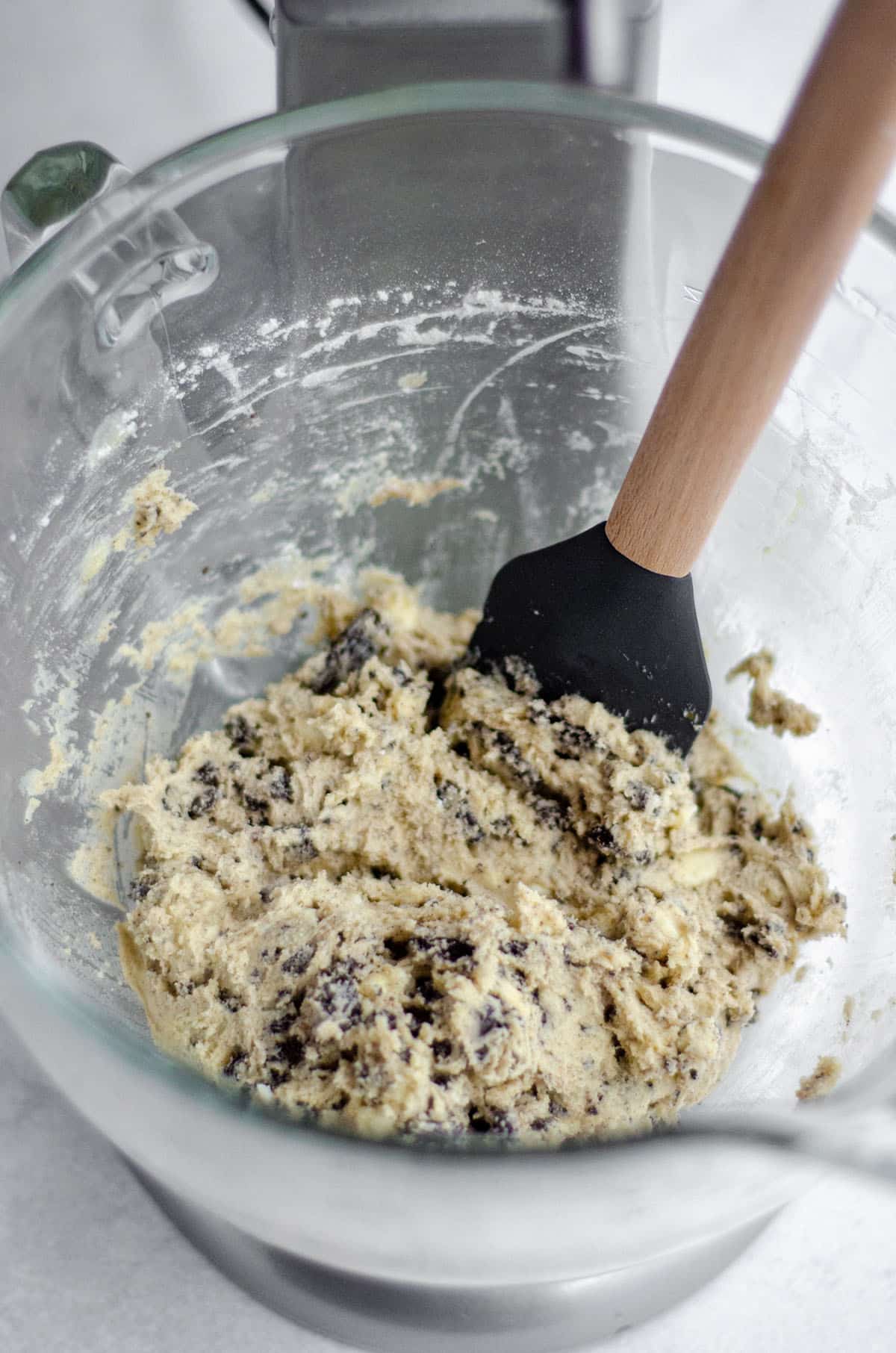 cookies and cream cookie dough in a glass bowl on a stand mixer with a spatula stuck in it