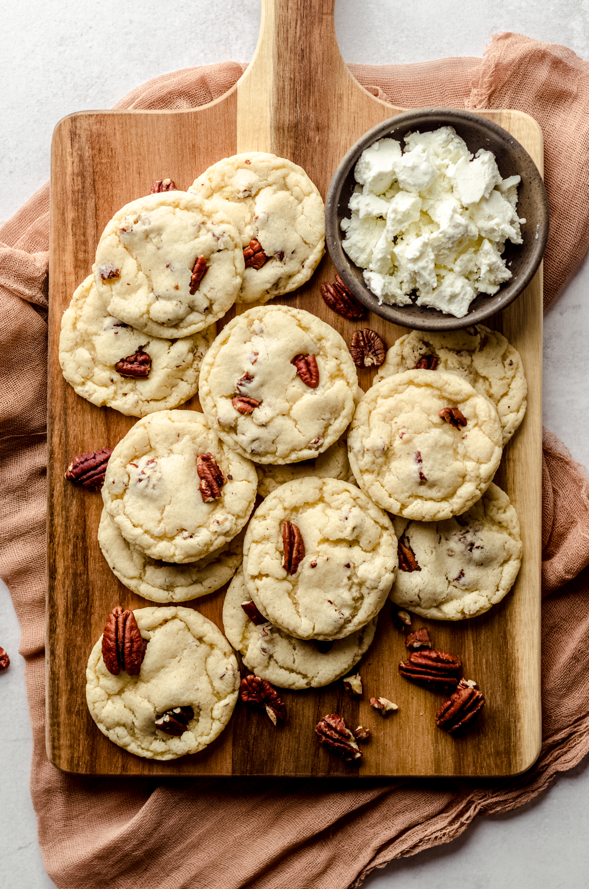 Aerial photo of maple pecan goat cheese sugar cookies on a wooden board with pecans and a bowl of goat cheese around them.