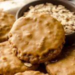 Molasses iced oatmeal cookies on a plate with a bowl of oats in the background.