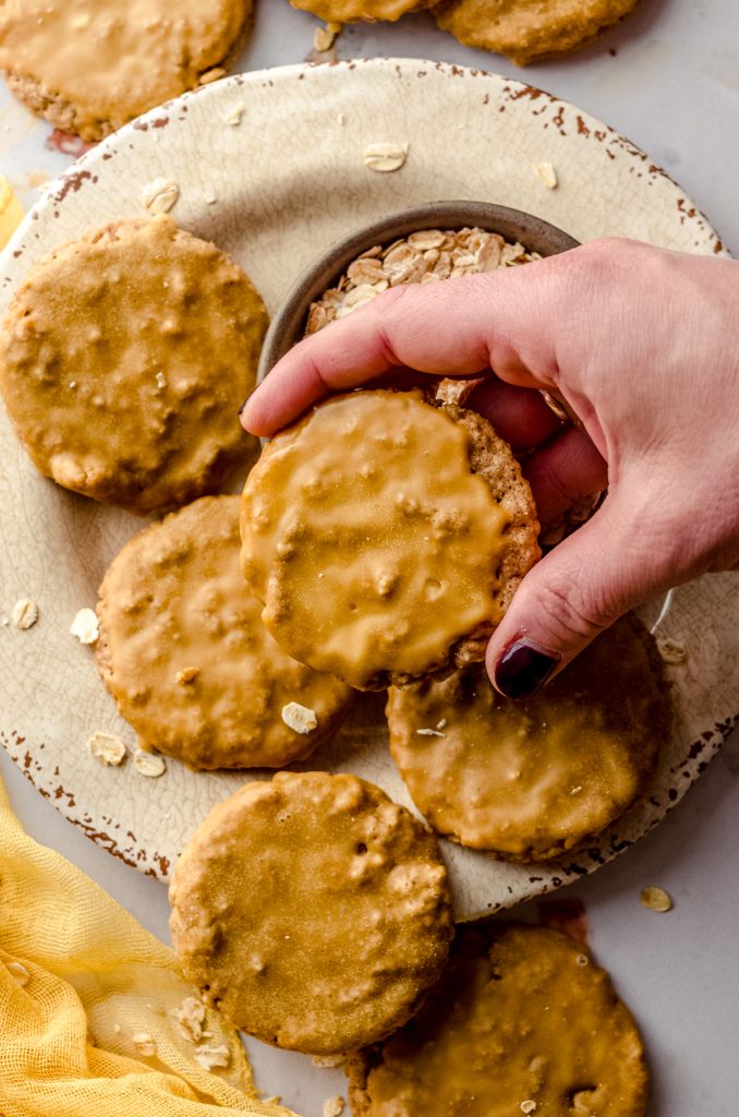 Aerial photo of someone holding a molasses iced oatmeal cookie above a a plate with a bowl of oats.