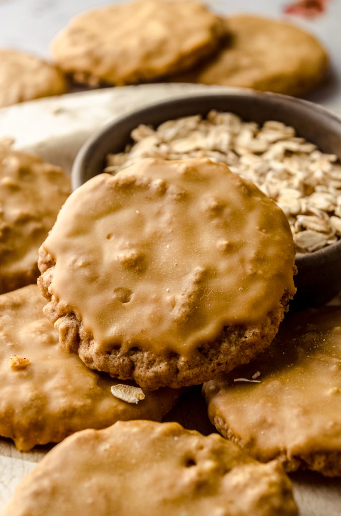 Molasses iced oatmeal cookies on a plate with a bowl of oats in the background.