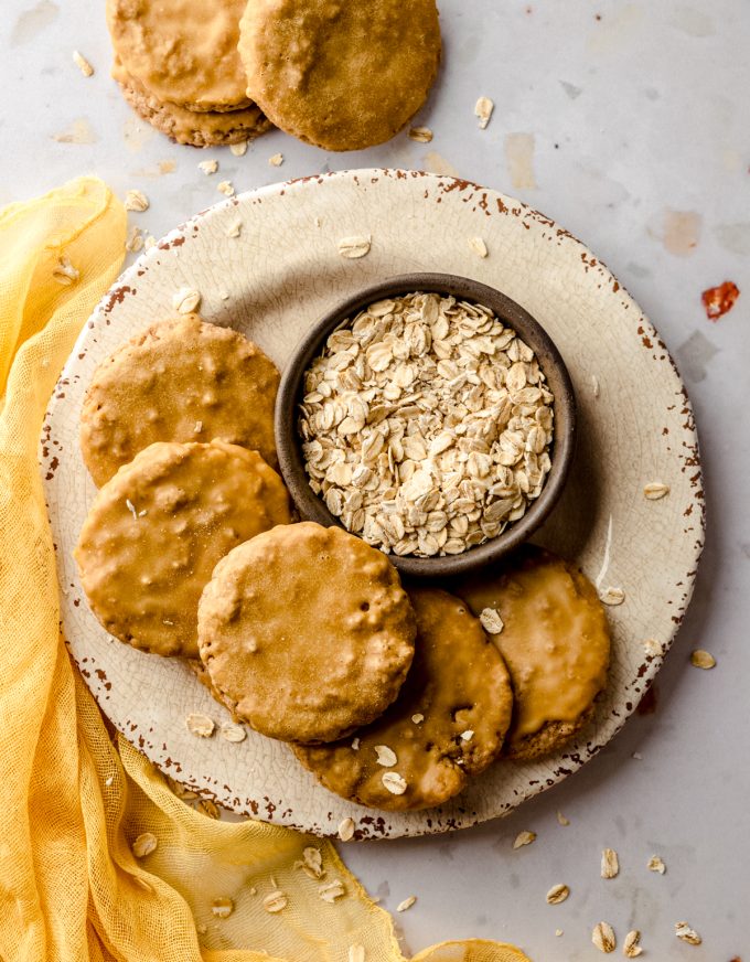 Aerial photo of molasses iced oatmeal cookies on a plate with a bowl of oats.