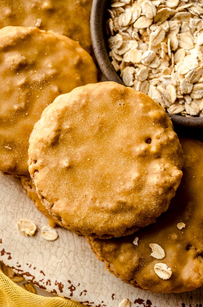 Aerial photo of molasses iced oatmeal cookies on a plate with a bowl of oats.