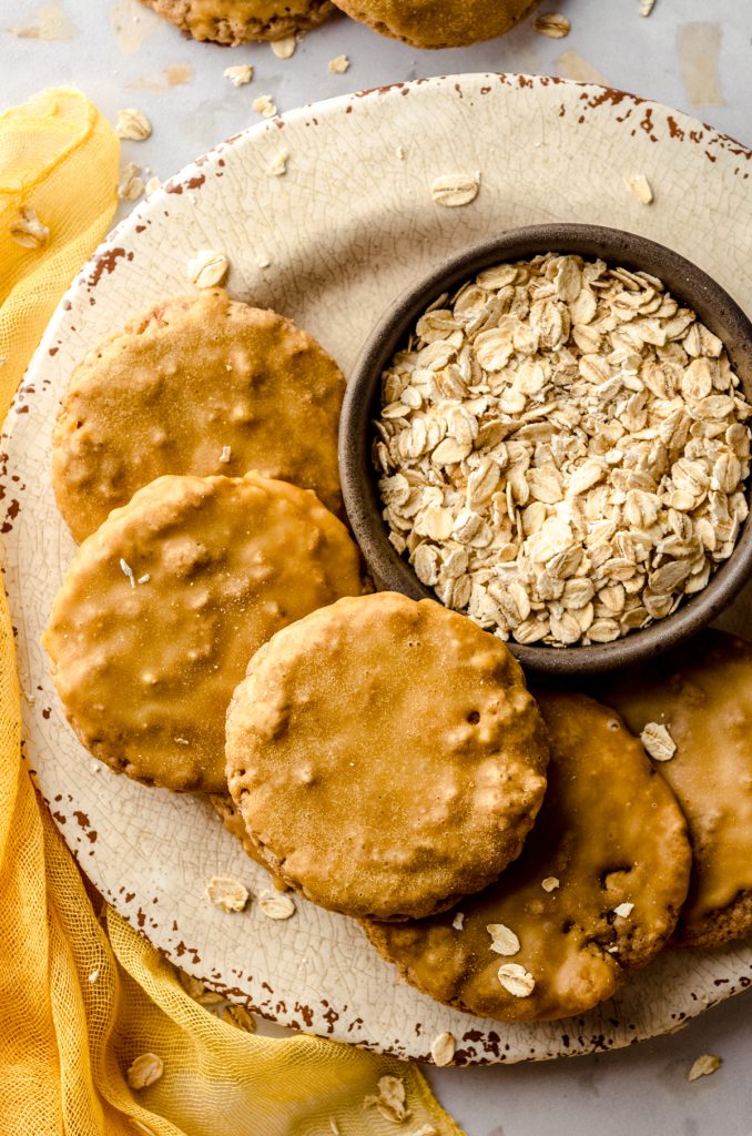 Aerial photo of molasses iced oatmeal cookies on a plate with a bowl of oats.