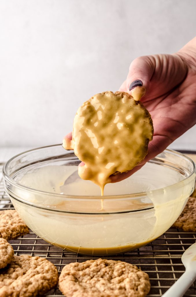 Someone is dipping an oatmeal cookie into a bowl of molasses icing.