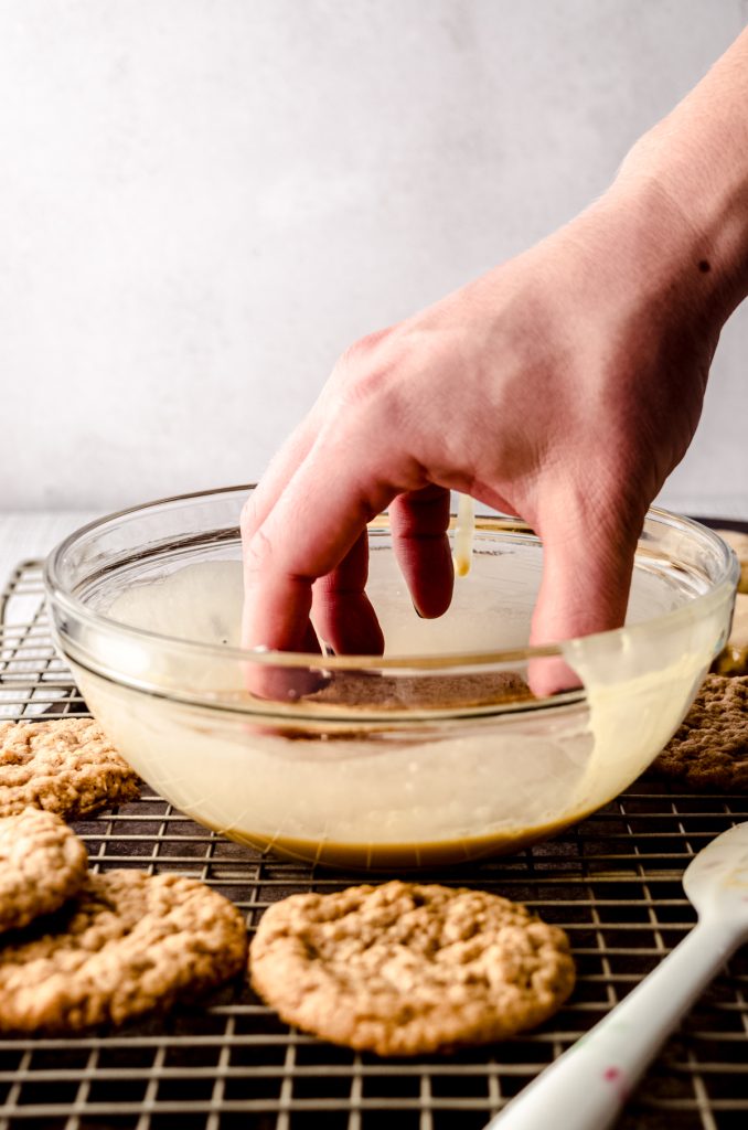 Someone is dipping an oatmeal cookie into a bowl of molasses icing.