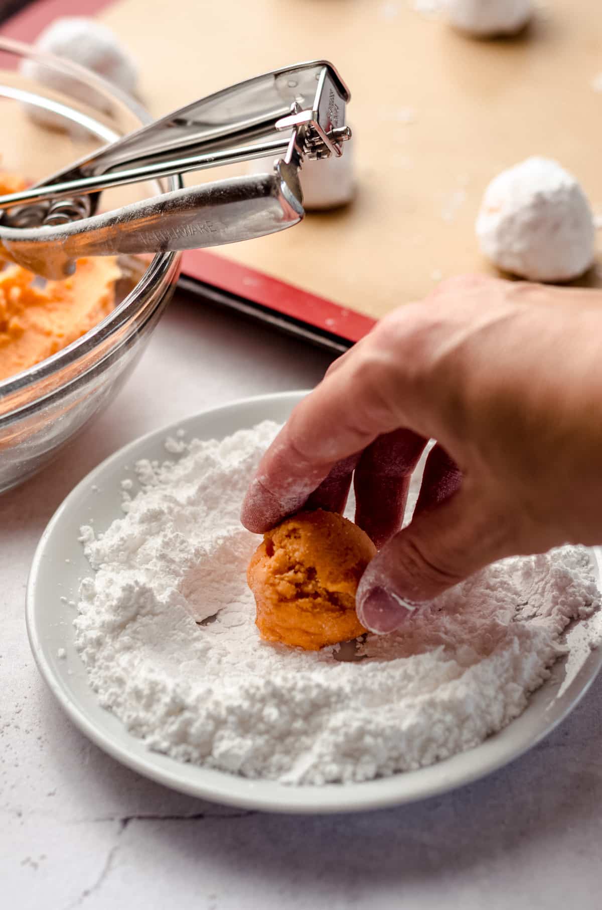 a hand rolling orange creamsicle cookie dough in powdered sugar to make crinkle style cookies