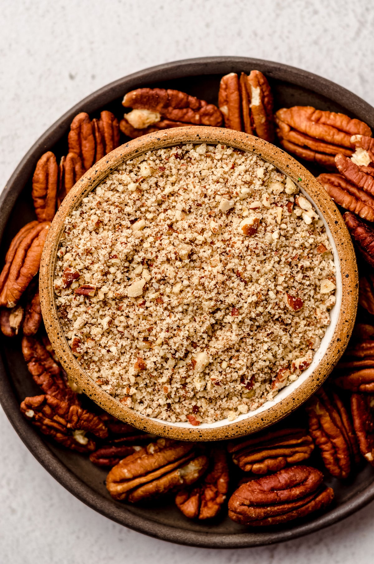 bowl of finely chopped pecans in a bowl on a plate with pecan halves