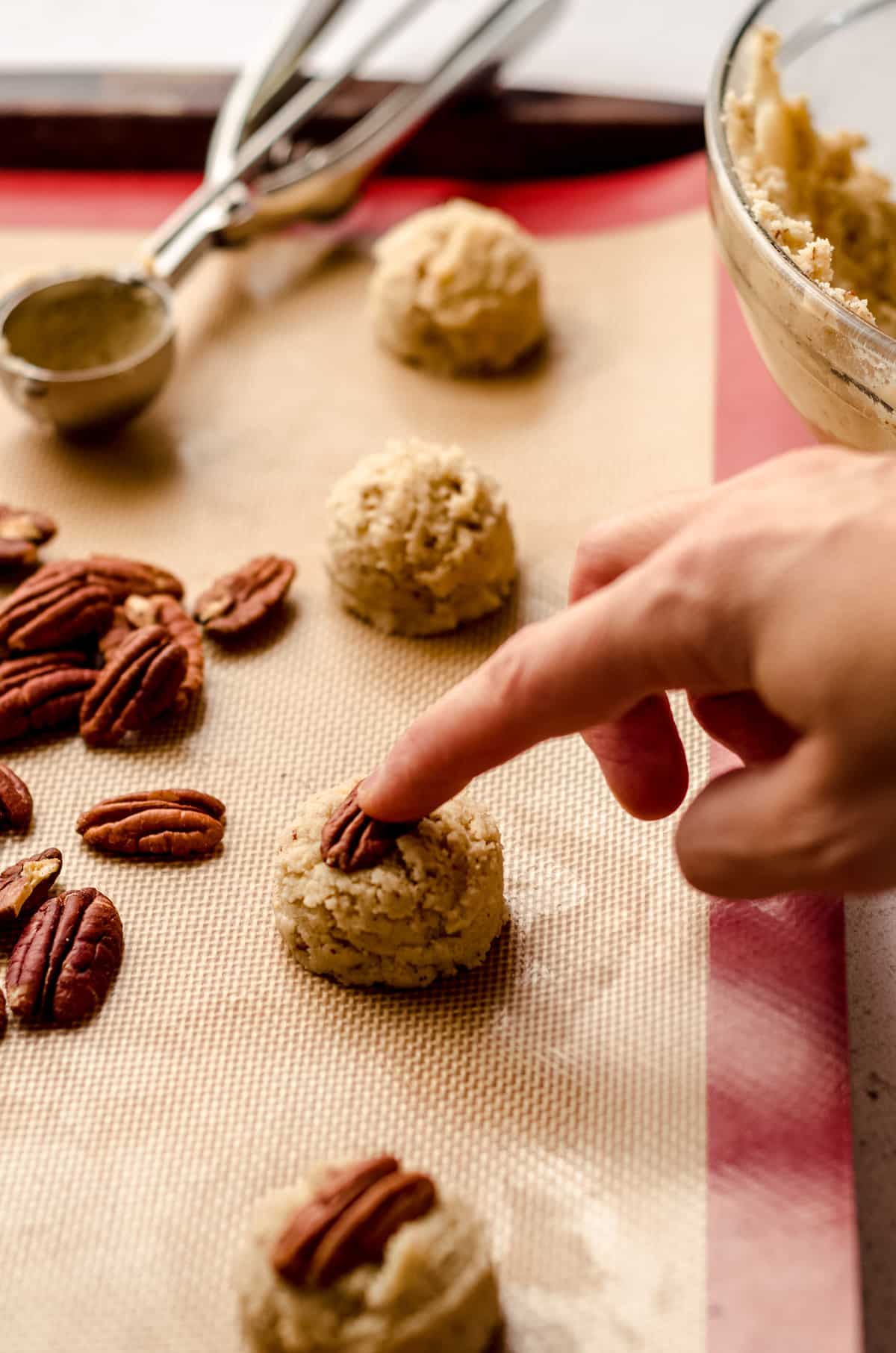 pressing a pecan half into the top of a pecan sandies cookie dough ball